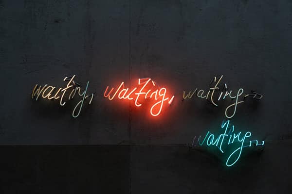 4 script signs on a wall with the word waiting in each, 1 illuminated in orange, another illuminated in blue