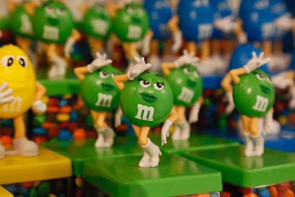 Green M&M's character mounted on a statue in a store, with many more in the background and other M&M's character statues as well