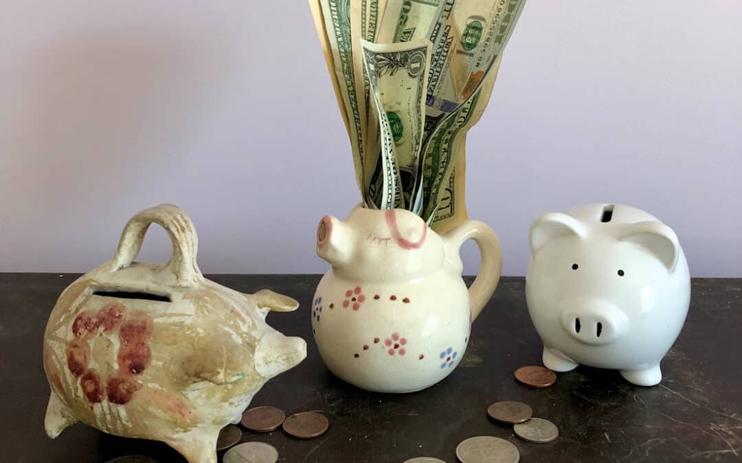 Two ceramic piggy banks and a small ceramic pig pitcher in a row on a wooden cabinet against a light lavender grey wall. US coins are scattered on the cabinet. A cluster of US paper currency in a variety of denominations sprout from the pig pitcher. Should you charge for your newsletter