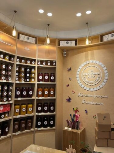 A section of the store La Chambre Aux Confitures in Paris, with its curved wall showing 3 shelving sections with 5 shelves each. Each shelf displays a flavor of jam. The jars are clear, letting the jam's red, yellow, or purple color come through.