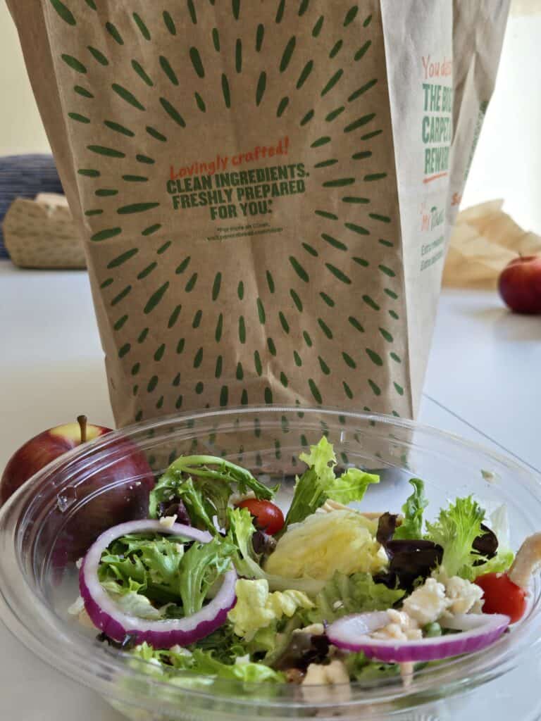 Panera paper bag saying “Lovingly crafted! Clean ingredients. Freshly prepared for you” with an apple and Fuji Apple chicken salad in front of it