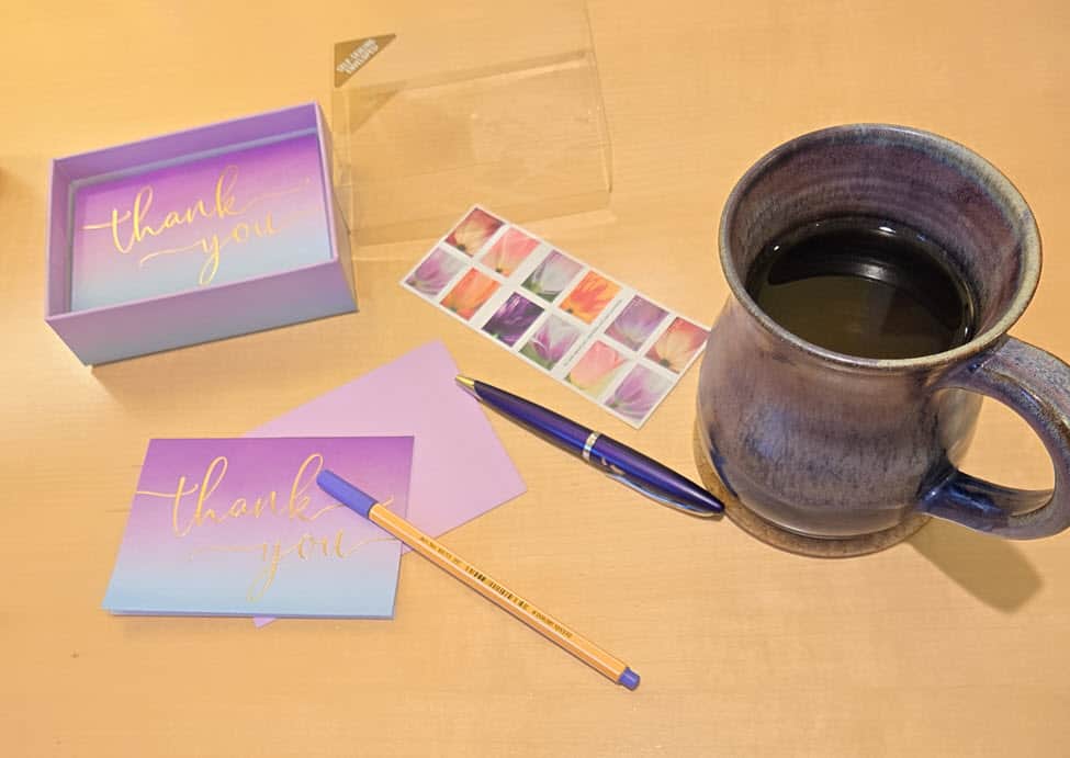 two purple and blue note cards with thank you in gold writing on the front, a purple mug of tea, a purple pen and a purple marker.
