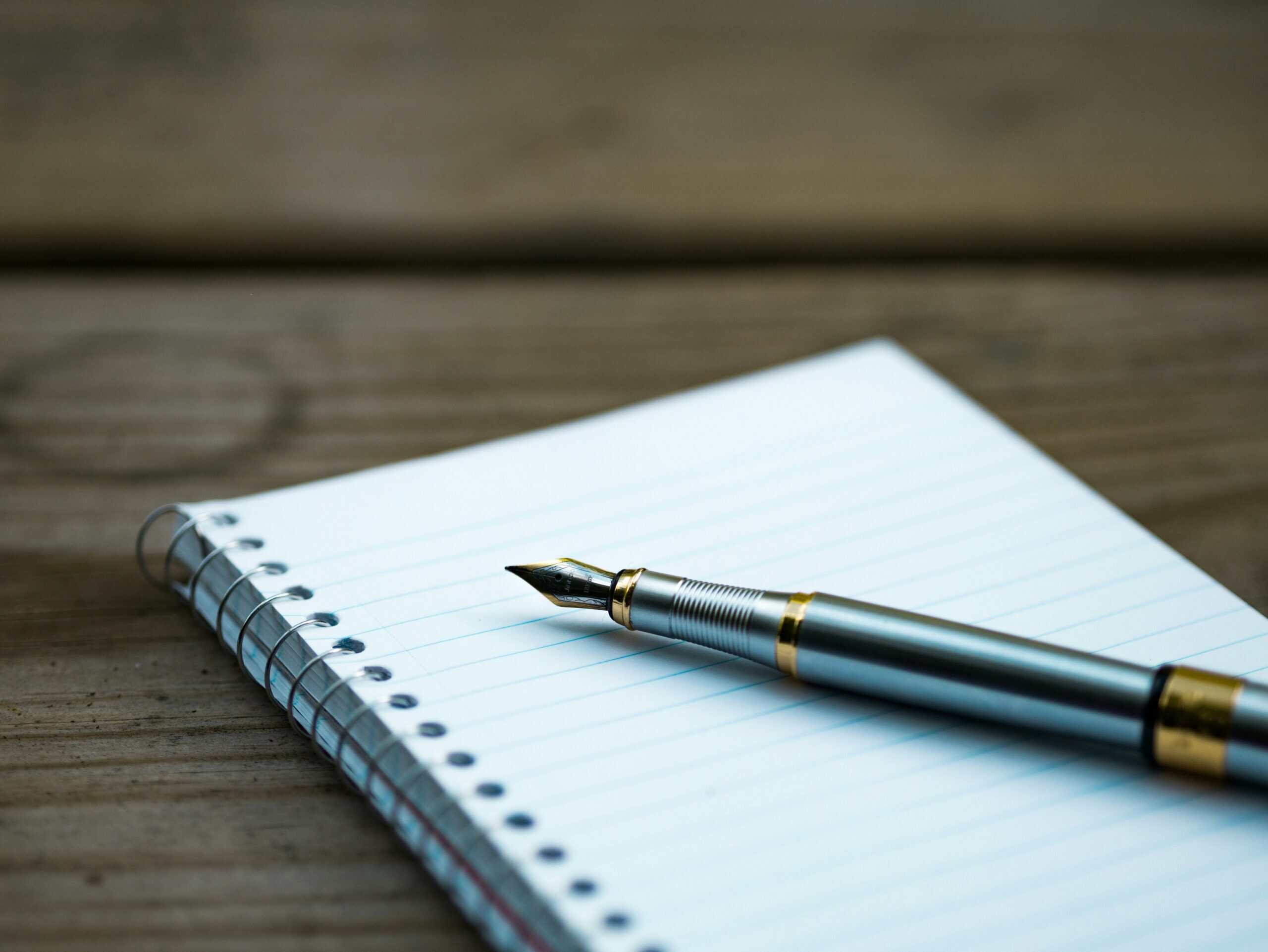 A quill pen resting on a blank, lined spiral note book page, blank because the inner critic tells the writer the thoughts are never good enough for paper